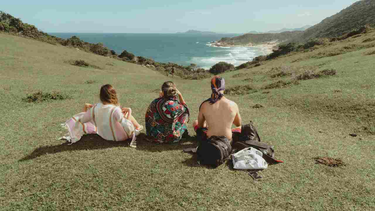 Tre ragazzi seduti in un prato di montagna che guardano il mare in lontananza
