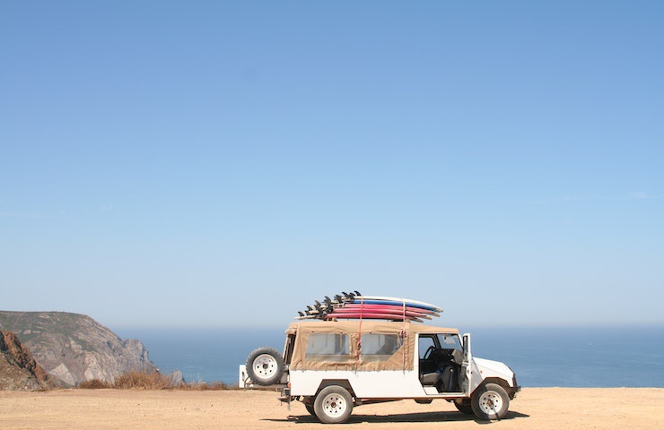 Jeep con tavole da surf appoggiate sul tetto e il mare come sfondo