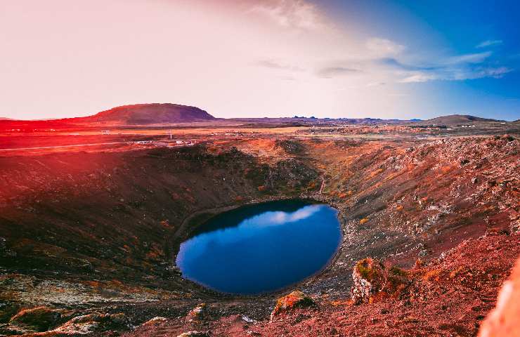 Panorama craterico con in mezzo un lago in fondo al cratere di un blu intenso circondato dal rosso della terra