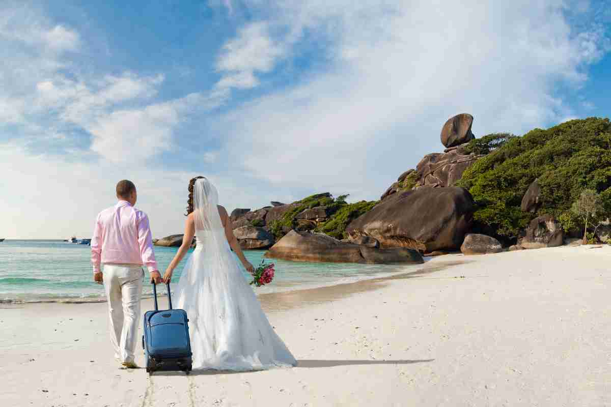 Sposi con valigia su una spiaggia paradisiaca