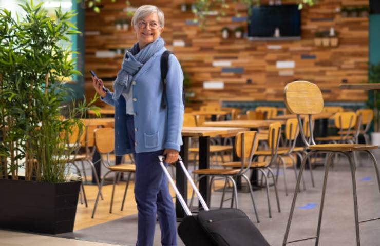 Donna anziana in aeroporto con una valigia pronta per partire