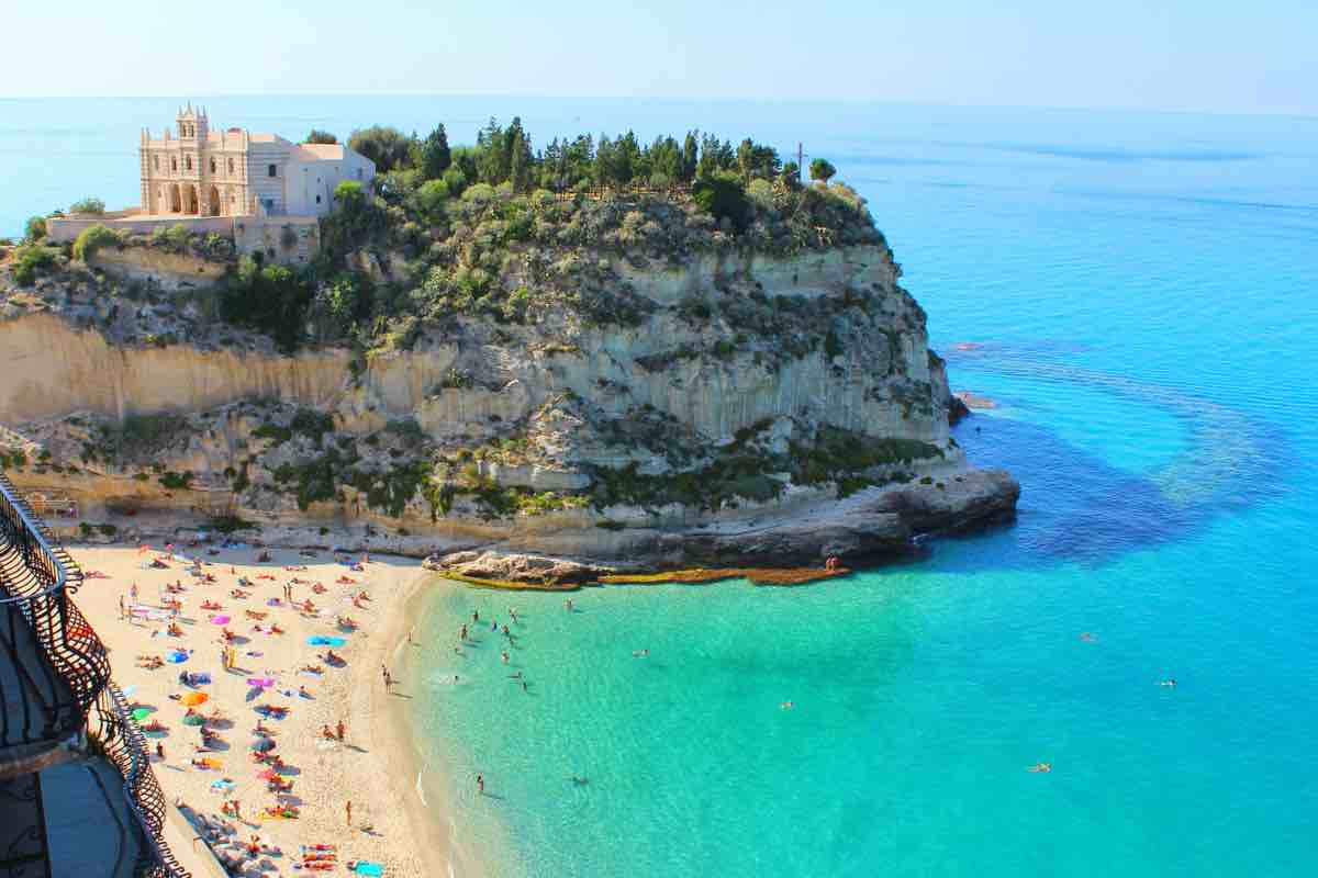 Spiaggia italiana con mare cristallino e promontorio sullo sfondo